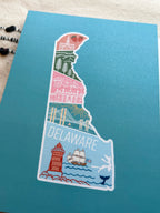 A postcard with an illustration of Delaware state in a colorful artistic style on a teal background.