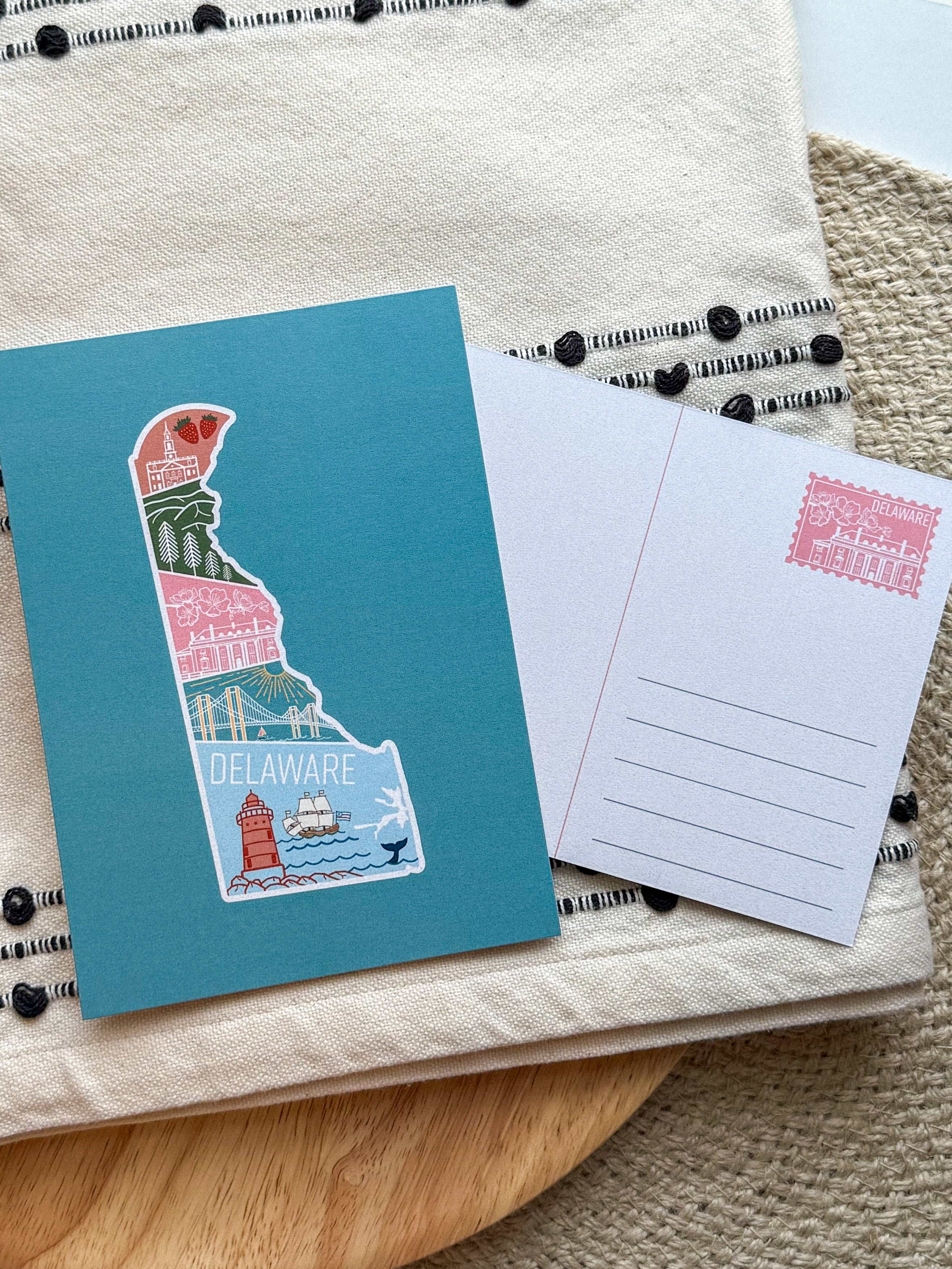 A postcard with an illustration of Delaware state in a colorful artistic style on a teal background.