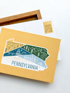 A postcard with an illustrated map of Pennsylvania, featuring a variety of colors and depicting landmarks and scenery.