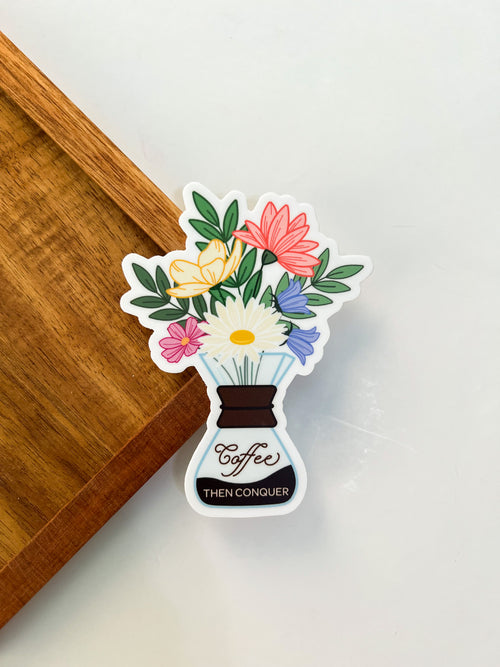 A vinyl sticker with a floral coffee chemex design layed on a wooden background. 
