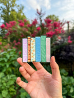 Colorful book-shaped bookmarks held in a hand with a garden background