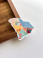 A vinyl sticker with an illustration of South Carolina state map colors and landmarks, placed on a wooden surface.