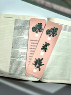 front and back rectangular bookmarks with rounded corners, featuring a green plant illustration and a Colossians 3:23-24 Bible verse, placed on a patterned fabric surface.