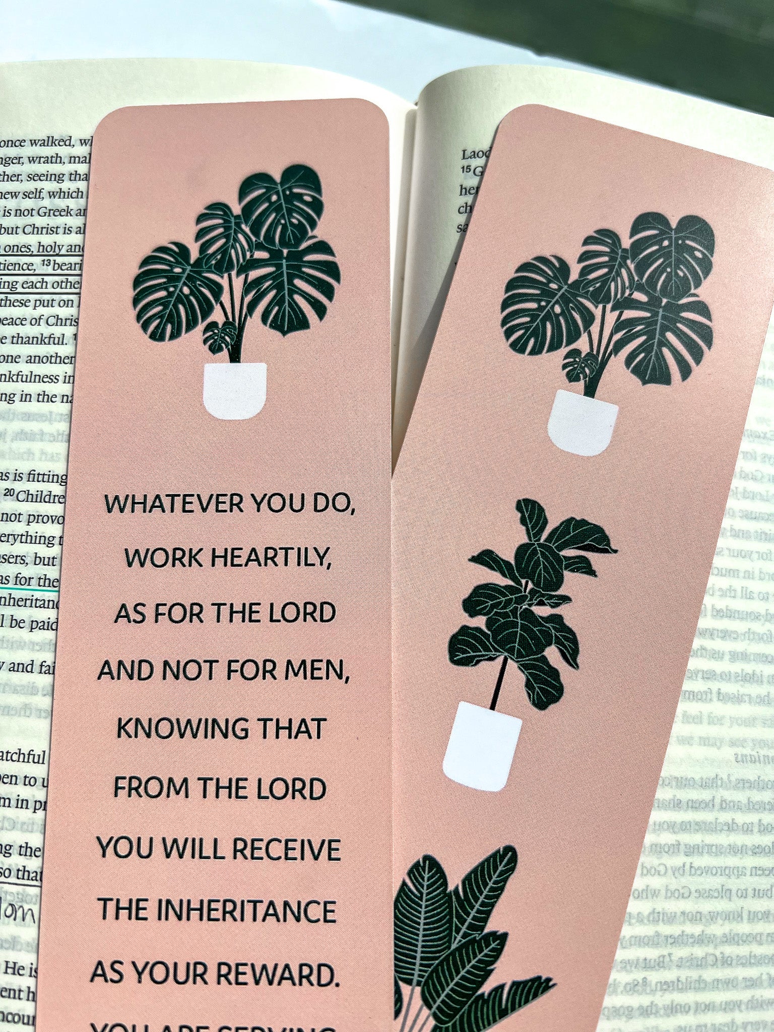 front and back rectangular bookmarks with rounded corners, featuring a green plant illustration and a Colossians 3:23-24 Bible verse, placed on a patterned fabric surface.