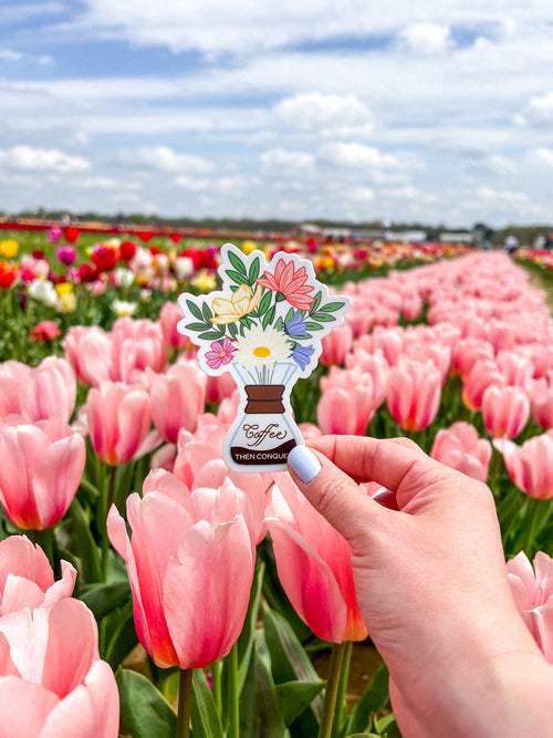 A vinyl sticker with a floral design being held by a hand, with a background of tulips in a field.