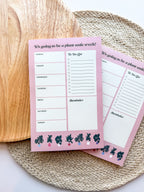A notepad with plant illustrations at the bottom, a pink background with text areas for notes, weekly schedule. placed on a woven mat.