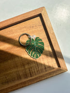An acrylic keychain with a green leaf design, attached to a metal keyring, displayed on a wooden surface.