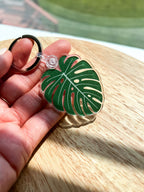 An acrylic keychain with a green leaf design, attached to a metal keyring, displayed on a wooden surface.