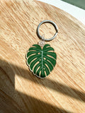 An acrylic keychain with a green leaf design, attached to a metal keyring, displayed on a wooden surface.