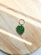 An acrylic keychain with a green leaf design, attached to a metal keyring, displayed on a wooden surface.