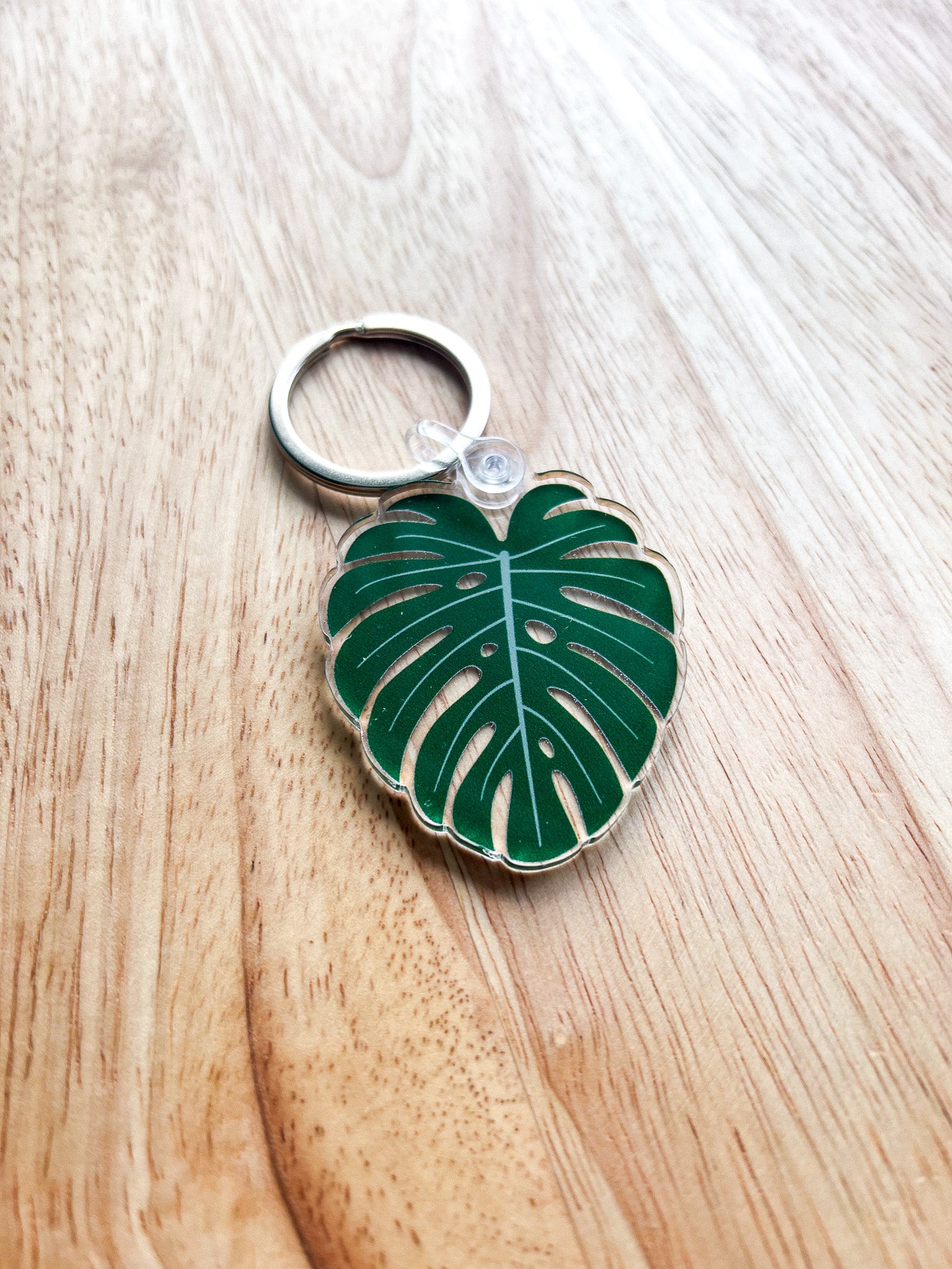 An acrylic keychain with a green leaf design, attached to a metal keyring, displayed on a wooden surface.