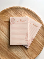 A floral tulip peachy pink lined notepad, placed on a wooden round surface