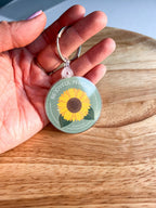 A double-sided acrylic keychain with a sunflower design on a wooden surface.
