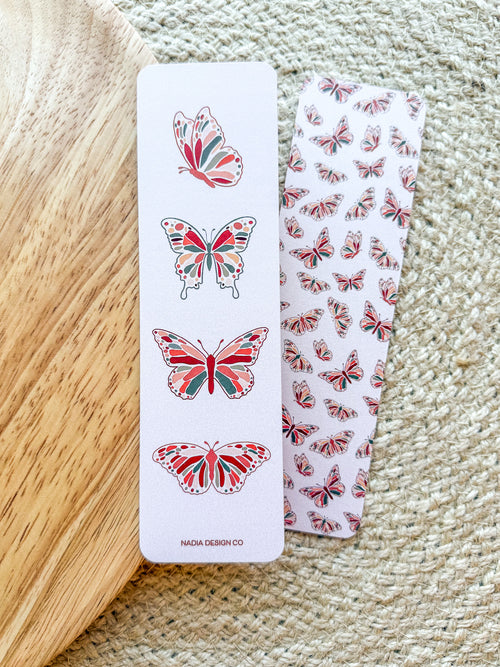 A bookmark with a double-sided illustration of butterflies, printed on pearl paper with a subtle shimmer, placed on an open book.