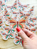 A person holding a clear vinyl sticker with a warm toned butterfly illustration.