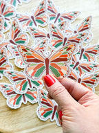 A person holding a clear vinyl sticker with a warm toned butterfly illustration.