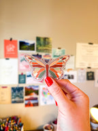 A person holding a clear vinyl sticker with a warm toned butterfly illustration.