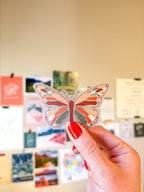 A person holding a clear vinyl sticker with a warm toned butterfly illustration.