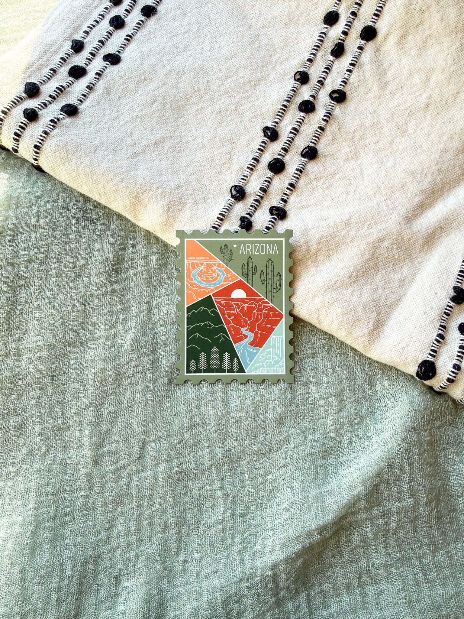 Colorful postage stamp design of Arizona held by a hand against a textured fabric background