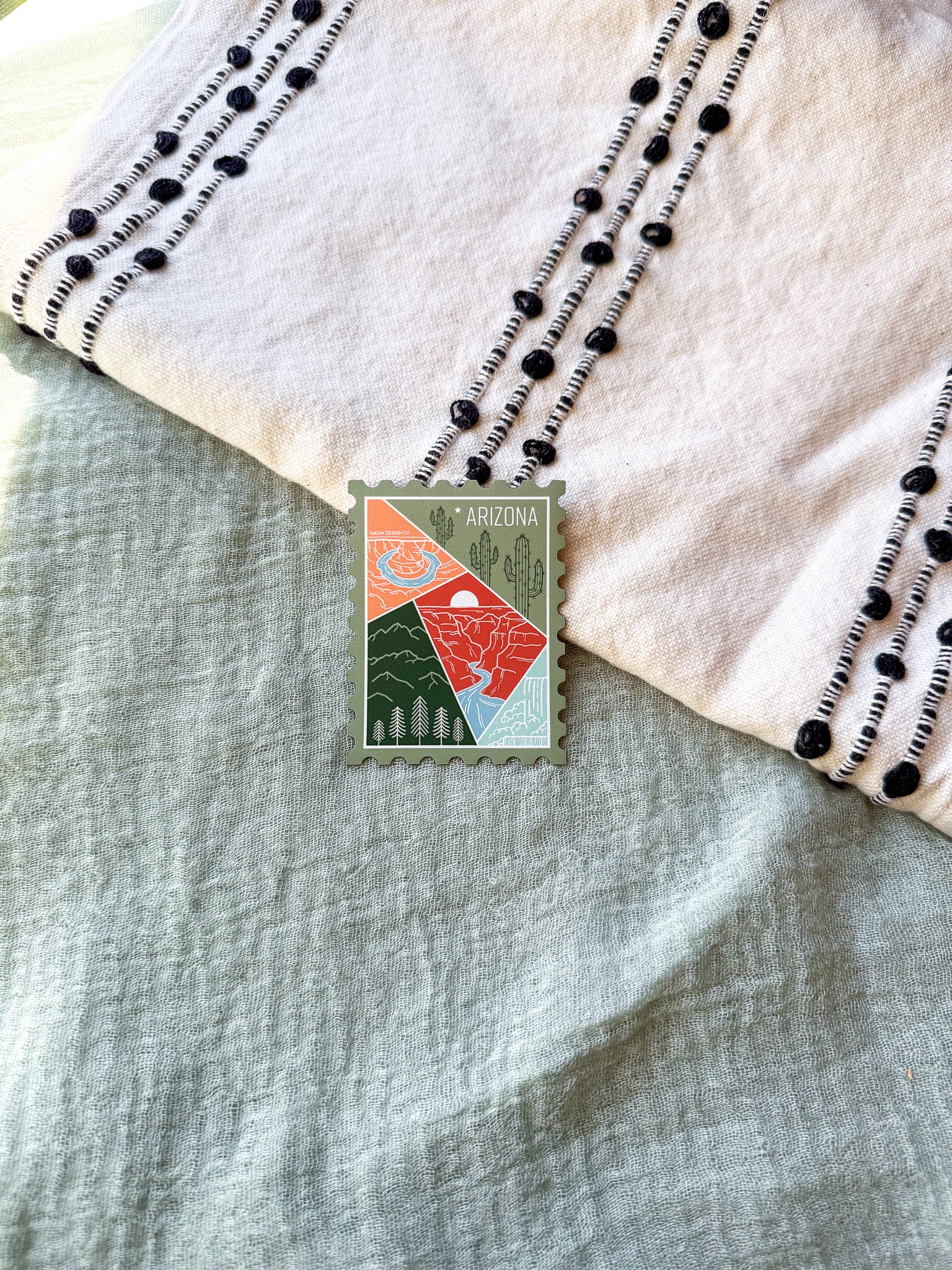 Colorful postage stamp design of Arizona held by a hand against a textured fabric background