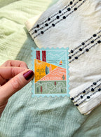 Hand holding a decorative California-stamp shaped themed postcard with texture background.