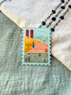 Hand holding a decorative California-stamp shaped themed postcard with textured background.