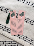 Two rectangular bookmarks with rounded corners, featuring a green plant illustration and a Colossians 3:23-24 Bible verse, placed on a patterned fabric surface.