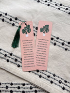 Two rectangular bookmarks with rounded corners, featuring a green plant illustration and a Colossians 3:23-24 Bible verse, placed on a patterned fabric surface.