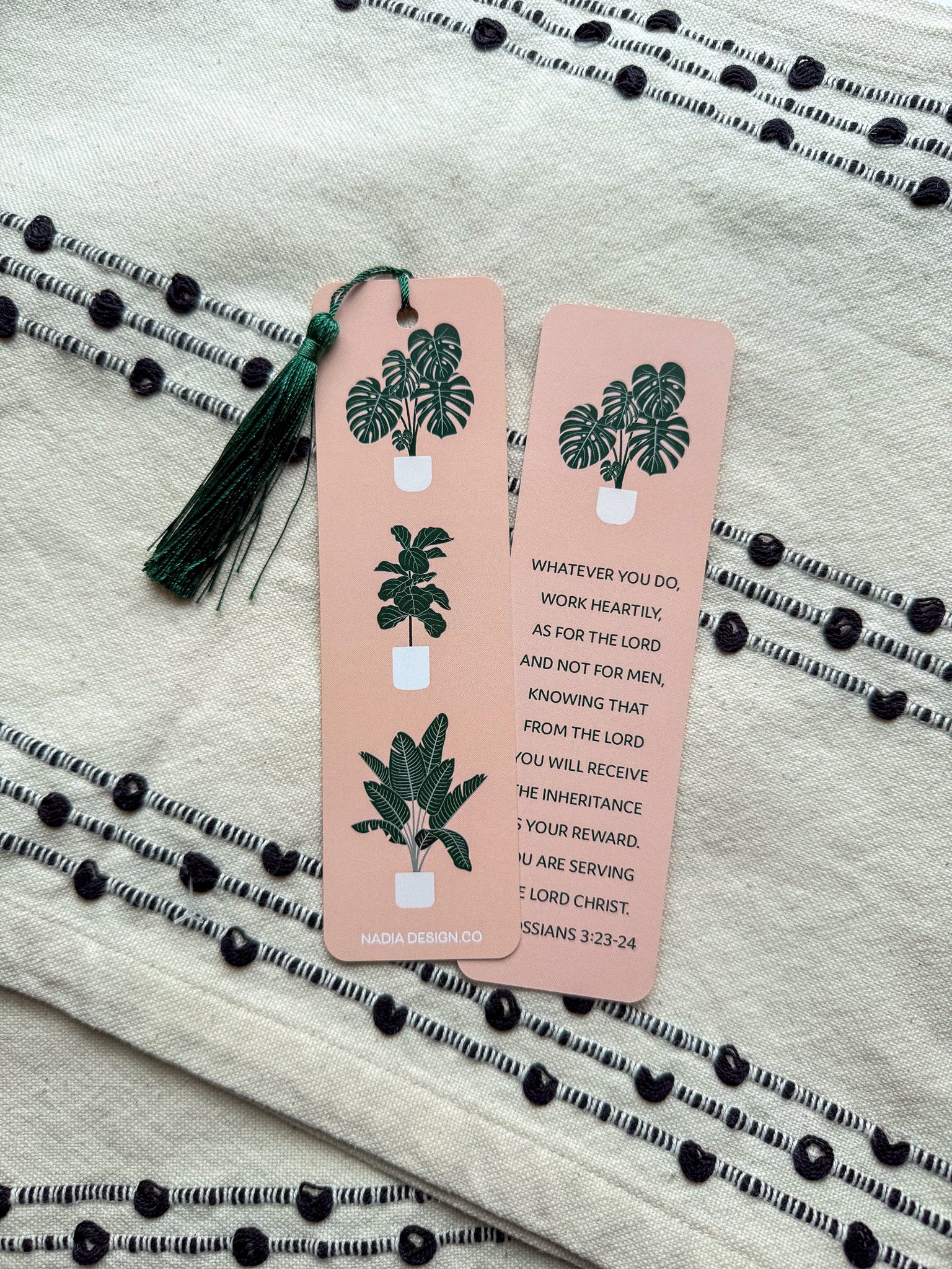 front and back rectangular bookmarks with rounded corners, featuring a green plant illustration and a Colossians 3:23-24 Bible verse, placed on a patterned fabric surface.
