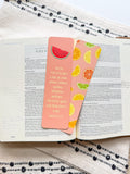 A pink bookmark with a tassel featuring a various fruit design and a Galatians 5:22-23 Bible verse, placed on a open bible. 