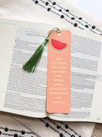 A pink bookmark with a tassel featuring a various fruit design and a Galatians 5:22-23 Bible verse, placed on a open bible. 