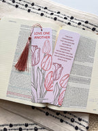 A bookmark with a floral design and a verse from the Bible John 15:12-13, held in a hand. The bookmark has a pearl paper finish with rounded corners.