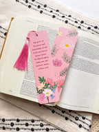 Two pink bookmarks with floral illustrations and a Bible verse written on them with a pink tassel, placed on a bible.
