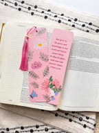 Two pink bookmarks with floral illustrations and a Bible verse written on them with a pink tassel, placed on a bible.