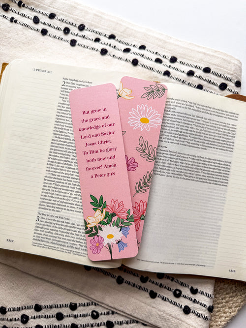 Two pink bookmarks with floral illustrations and a Bible verse written on them, placed on a bible.