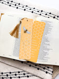A yellow bookmark with a bee illustration and honeycomb pattern, titled 'Proverbs 16:24 Bible Verse', placed on an open book.