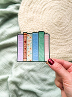 Colorful book-shaped bookmarks held by a hand against a textured fabric background