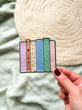 Colorful book-shaped bookmarks held by a hand against a soft fabric background