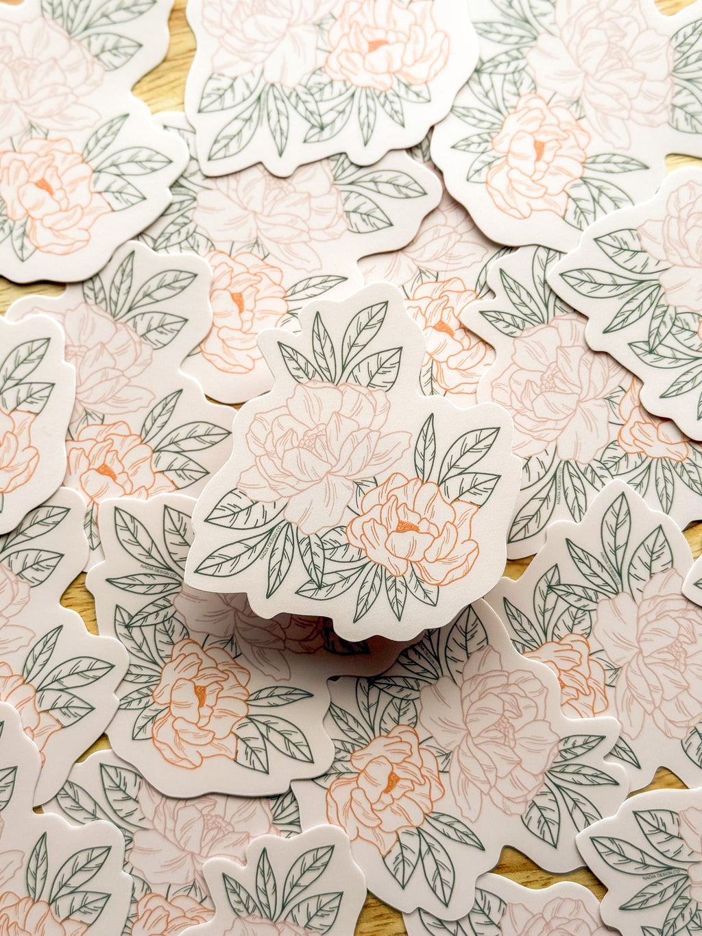 A hand holding a vinyl sticker with a illustrated peony design.