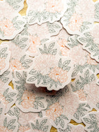 A hand holding a vinyl sticker with a illustrated peony design.