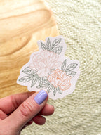 A hand holding a vinyl sticker with a illustrated peony design.