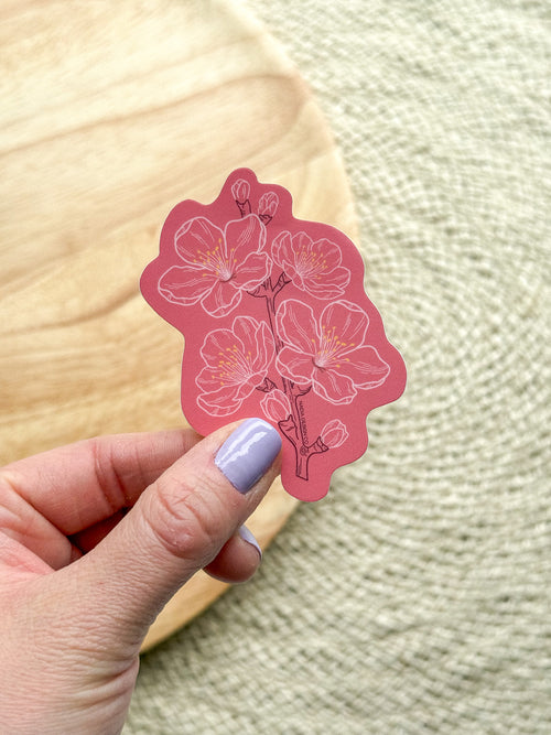 A vinyl sticker with a pink cherry blossom design being held by a hand.