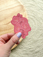 A vinyl sticker with a pink cherry blossom design being held by a hand.