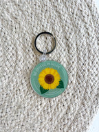 A double-sided acrylic keychain with a sunflower design on a wooden surface.