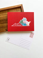A postcard with an illustration of Virginia state landmarks on a red background with the word 'Virginia' written across the lower part of the state outline.