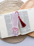 A bookmark with a rose illustration and a red tassel, placed on an open book.