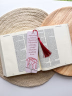 A bookmark with a rose illustration and a red tassel, placed on an open book.