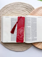 A bookmark with a rose illustration and a red tassel, placed on an open book.
