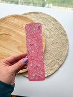 hand holding pink cherry blossom illustrated floral bookmarks on a wooden and woven surface