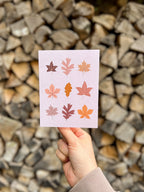 illustrated fall leaves greeting card held up by a hand with wooden background. 
